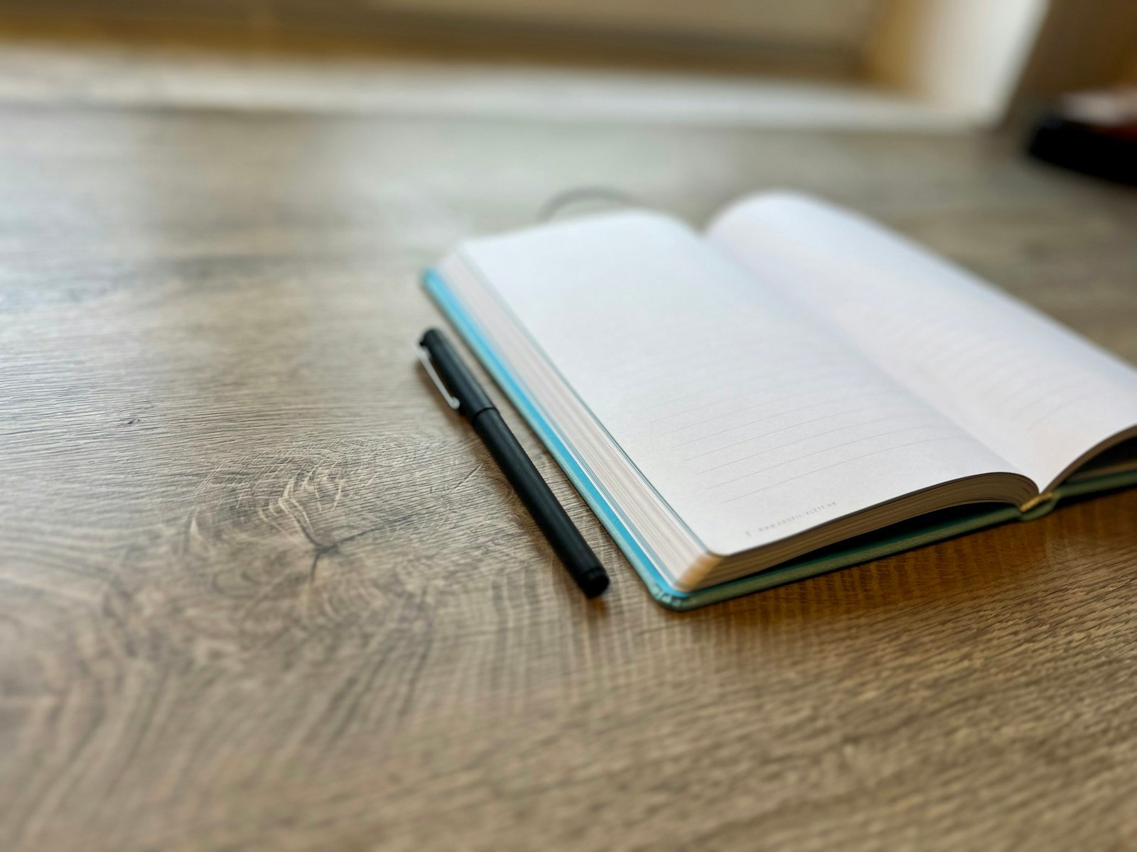 An open notebook and pen on a warm wooden desk.