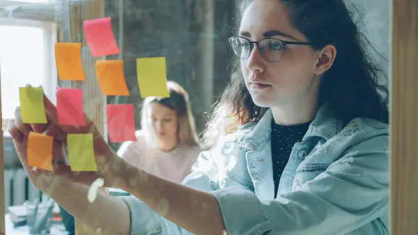 A student arranging colourful sticky notes on a glass wall.