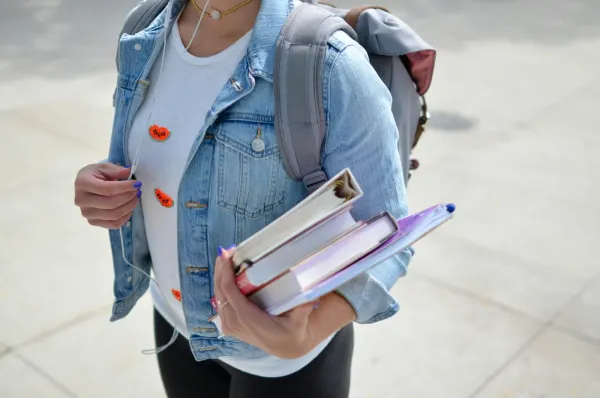 A student with a backpack carrying a stack of books and folders.